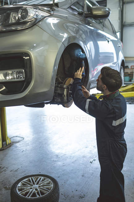 Male mechanic examining a car with torch in repair garage — Stock Photo