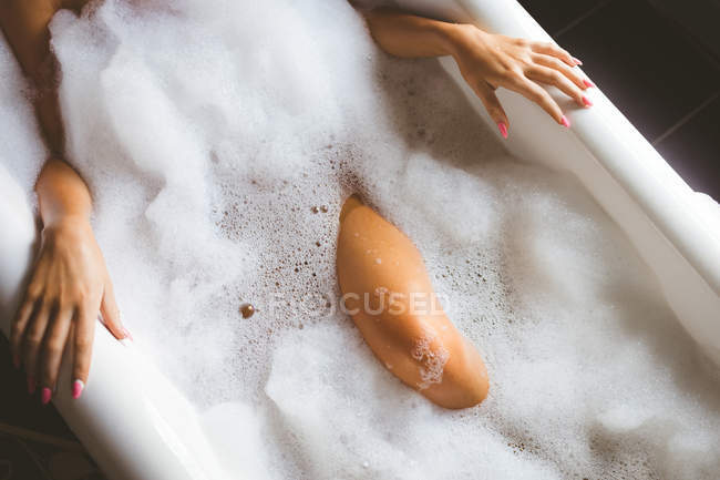 Средняя секция женщины, принимающей пенную ванну в ванной комнате дома — стоковое фото