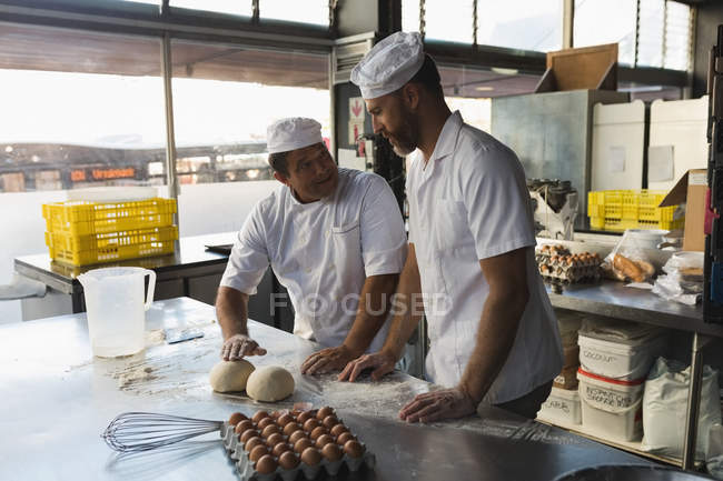 Male baker preparing dough with his coworker in bakery shop — Stock Photo