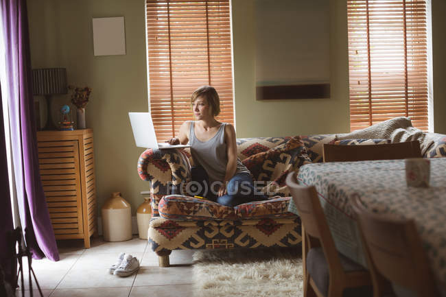 Красива жінка використовує ноутбук на дивані у вітальні вдома — стокове фото