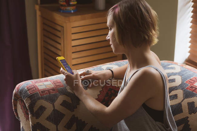 Красива жінка використовує мобільний телефон на дивані у вітальні вдома — стокове фото