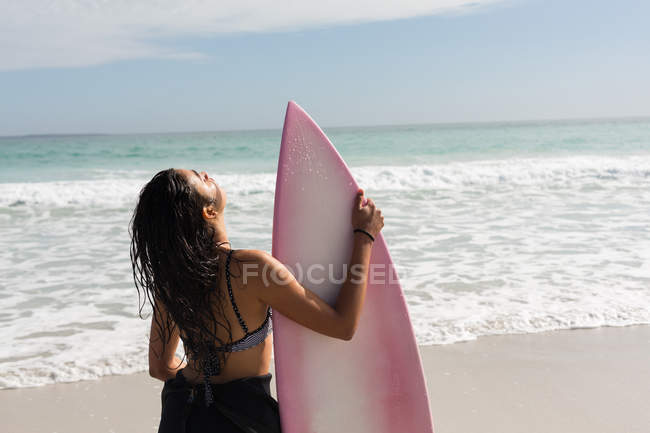 Vue arrière de surfeuse debout avec planche de surf sur la plage — Photo de stock