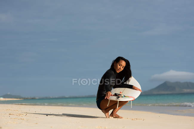 Frau kauert an einem sonnigen Tag mit Surfbrett am Strand — Stockfoto