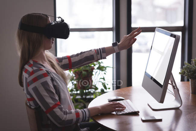 Женщина-руководитель, использующая гарнитуру виртуальной реальности с компьютером за столом в офисе — стоковое фото