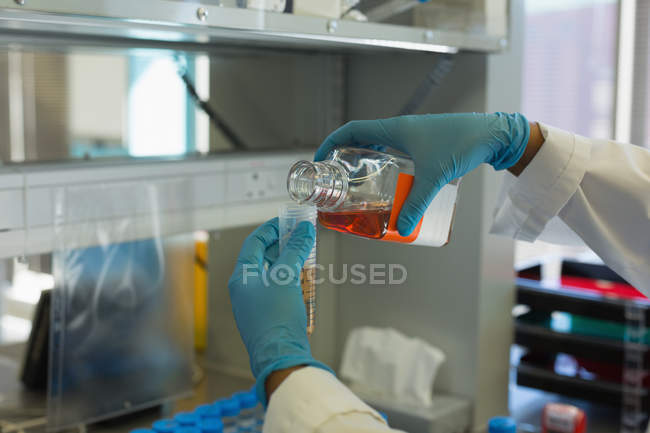 Científico vertiendo solución química en tubo de ensayo de la botella en el laboratorio - foto de stock