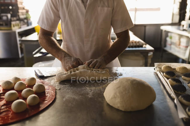 Sección media del panadero masculino preparando masa en la panadería - foto de stock