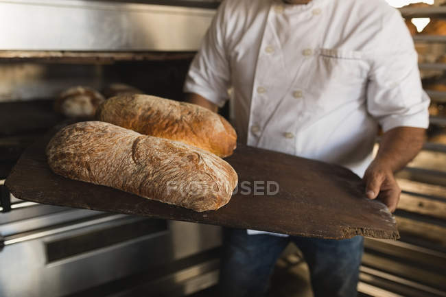 Mid section of male baker holding baked bread in bakery shop — Stock Photo
