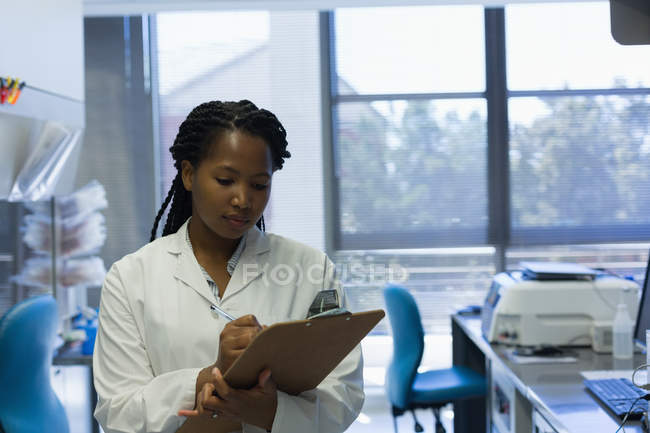 Cientista feminina escrevendo na área de transferência no laboratório — Fotografia de Stock