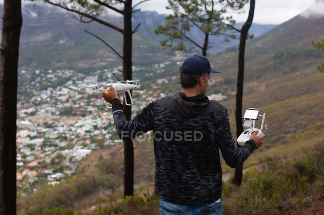 Rear view of man operating a flying drone in countryside — Stock Photo