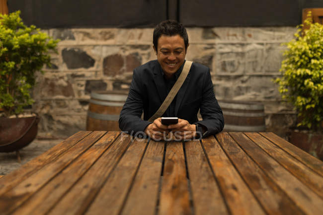 Empresário sorrindo usando telefone celular no café pavimento — Fotografia de Stock