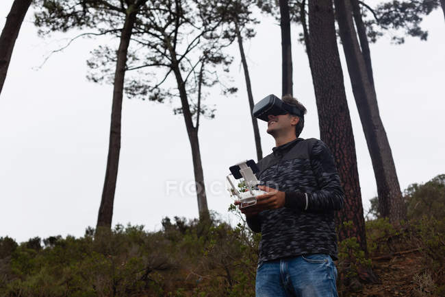 Людина, що керує літаючим безпілотником, використовуючи гарнітуру віртуальної реальності в сільській місцевості — стокове фото