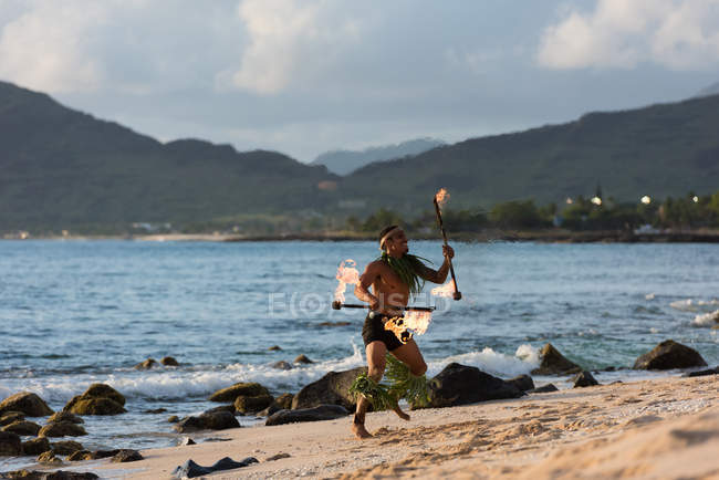 Male fire dancer performing with fire levi sticks at beach — Stock Photo