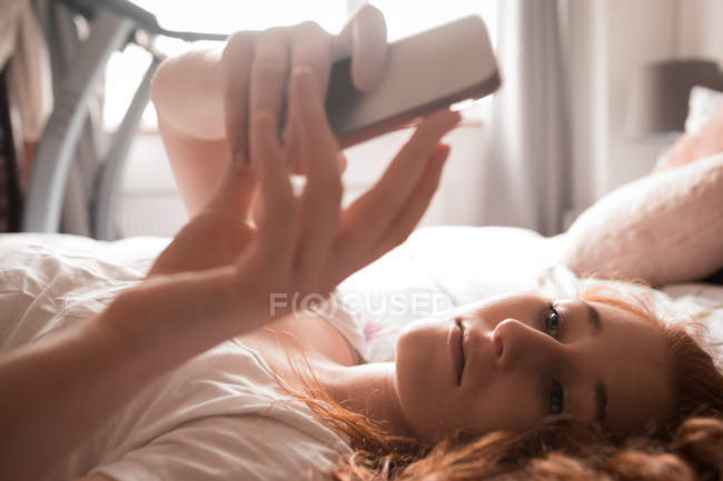 Жінка, що використання мобільного телефону у спальні будинку — стокове фото
