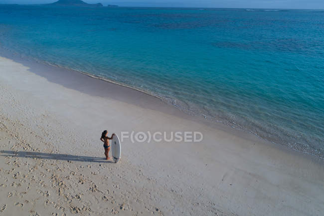 Жінка з дошкою для серфінгу стоїть на пляжі і дивиться море — стокове фото