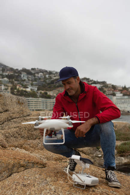 Hombre operando un dron volador en una roca - foto de stock