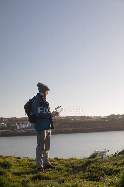 Male hiker operating drone near lake at countryside — Stock Photo