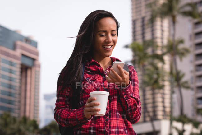 Sorrindo mulher bonita usando telefone celular enquanto toma café na rua — Fotografia de Stock