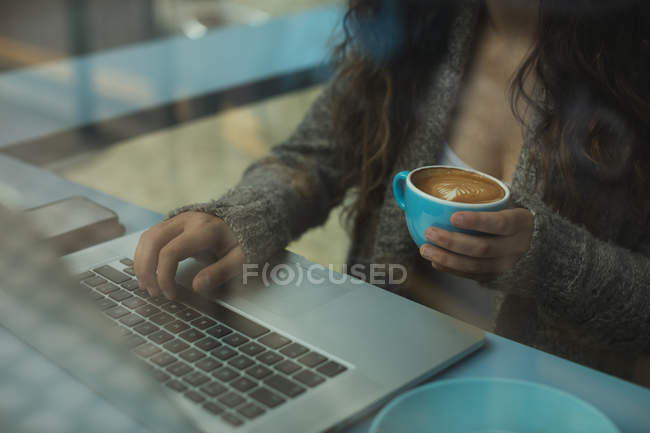 Mid section of woman using laptop while having coffee in coffee shop — Stock Photo