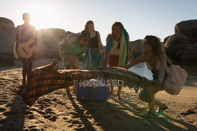 Groupe d'amis posant une couverture de pique-nique sur la plage — Photo de stock