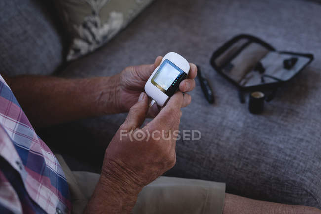 Старший мужчина проверяет сахар в крови с помощью глюкометра дома — стоковое фото