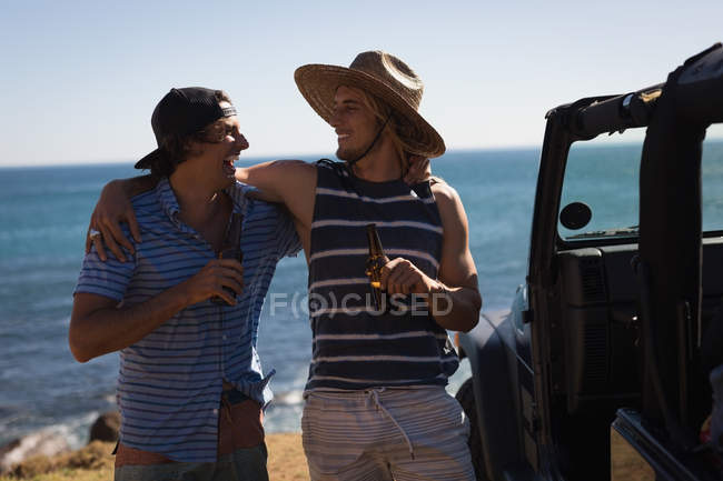 Amigos varones tomando cerveza en la playa en un día soleado - foto de stock