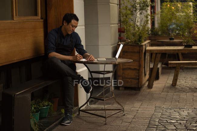 Homme d'affaires écrit sur le journal avec ordinateur portable sur la table au café trottoir — Photo de stock