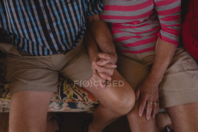 Romántica pareja de ancianos tomados de la mano en la sala de estar en casa - foto de stock