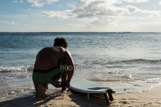 Male surfer tying surfboard leash on his leg at beach — Stock Photo