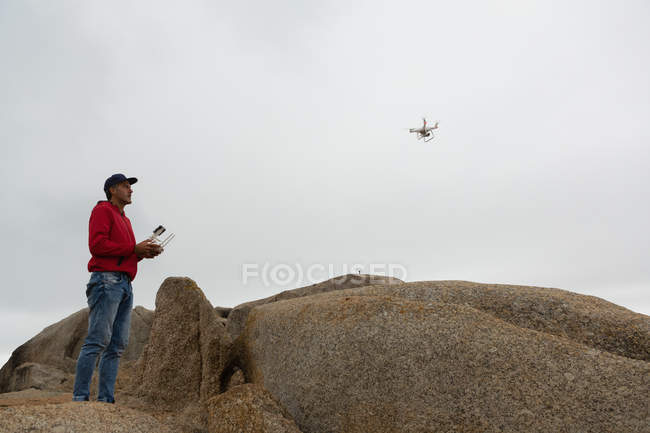 Человек, управляющий летающим дроном на камне — стоковое фото
