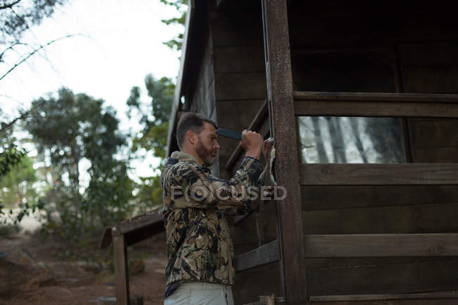 Side view of man nailing animal fur on log cabin — Stock Photo