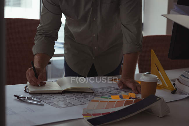 Seção intermediária do arquiteto escrevendo nota sobre diário no escritório — Fotografia de Stock