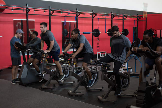 Jeunes athlètes faisant de l'exercice sur des vélos d'appartement dans un gymnase — Photo de stock