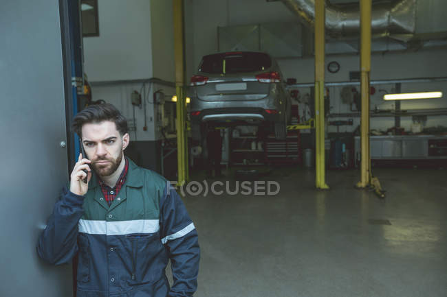 Mecánico hablando en un teléfono móvil en el garaje de reparación - foto de stock