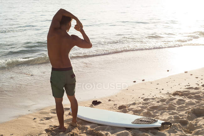 Vista trasera del surfista masculino haciendo ejercicio en la playa - foto de stock