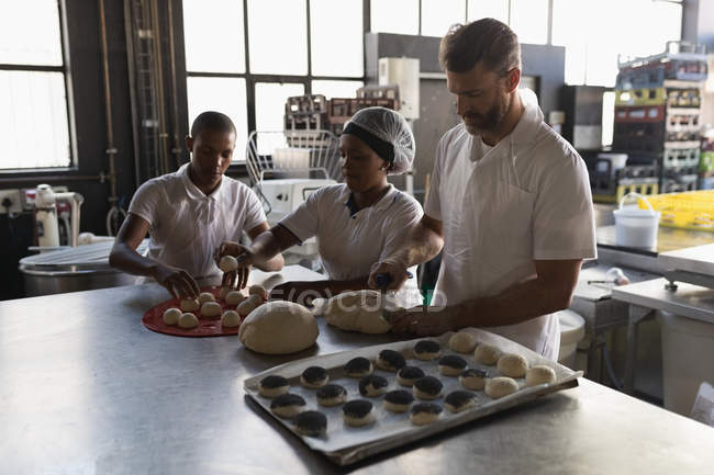 Male baker with coworkers preparing dough in bakery shop — Stock Photo