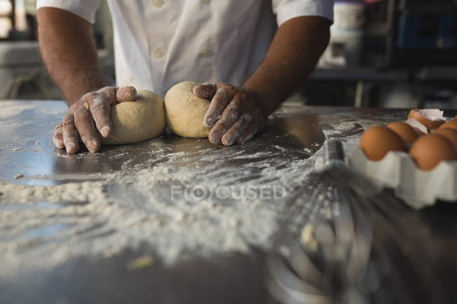 Sección media del panadero masculino preparando masa en la panadería - foto de stock
