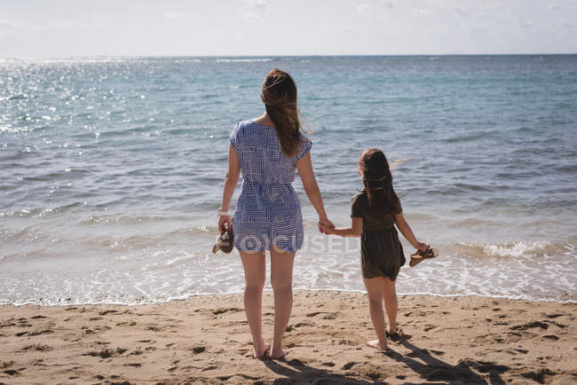 Вид ззаду мати і дочка тримають руки на пляжі — стокове фото