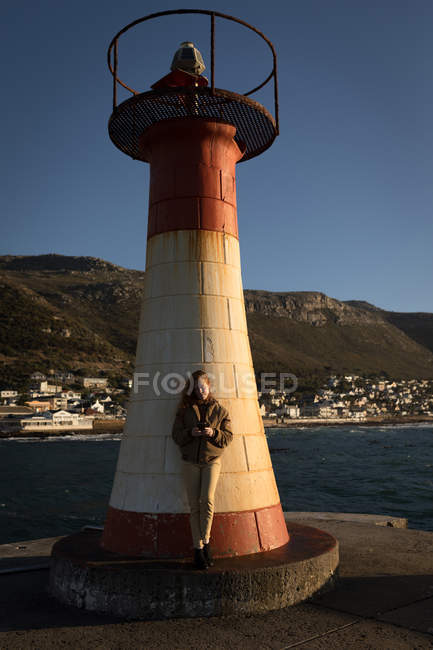 Belle femme utilisant un téléphone mobile près du phare — Photo de stock