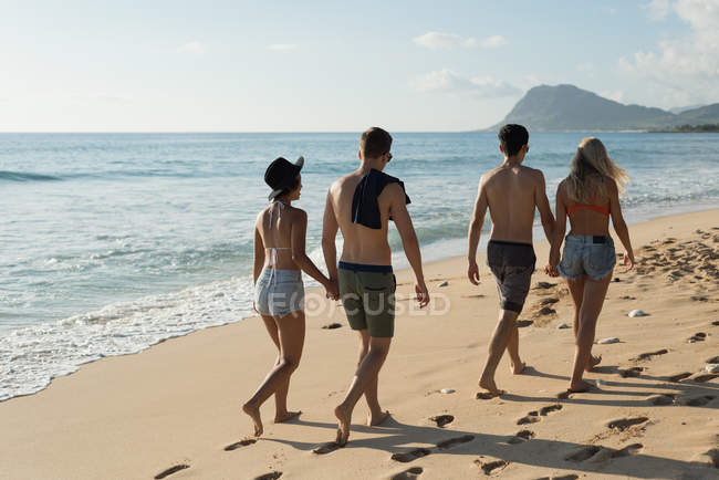 Две пары, идущие рука об руку на пляже — стоковое фото