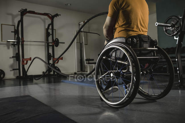 Handicapped man on wheelchair exercising with battle ropes in gym — Stock Photo