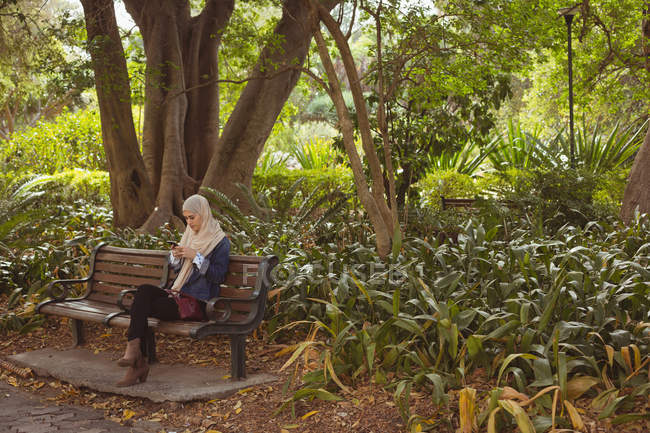 Hijab mulher sentada no banco e usando telefone celular no jardim — Fotografia de Stock