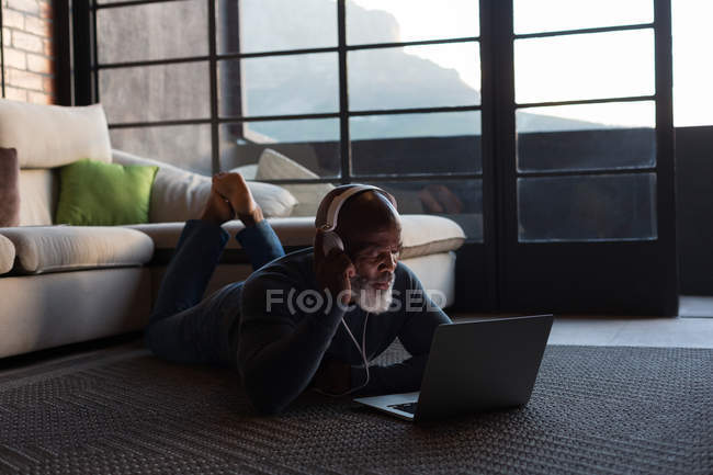 Homem sênior ouvindo música no laptop em casa — Fotografia de Stock