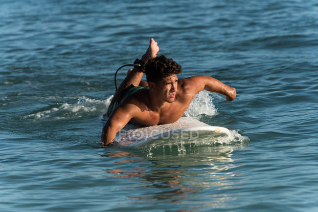 Surfista masculino surfeando con tabla de surf en el mar en un día soleado - foto de stock