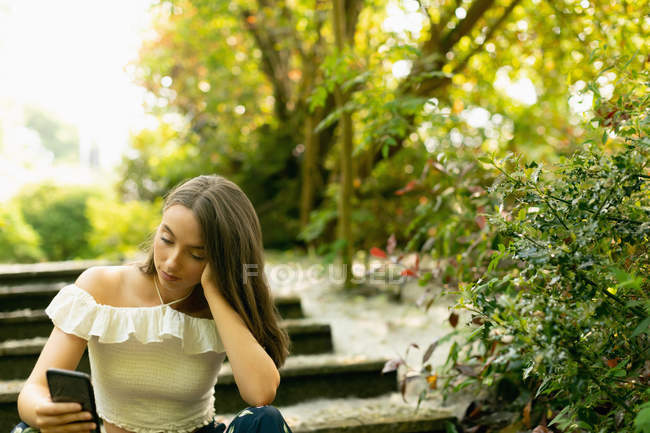 Beautiful woman using sitting on the steps and using her phone in the forest — Stock Photo