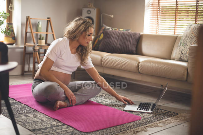 Вагітна жінка використовує ноутбук у вітальні вдома — стокове фото
