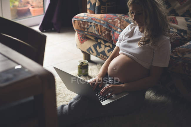Вагітна жінка використовує ноутбук у вітальні вдома — стокове фото