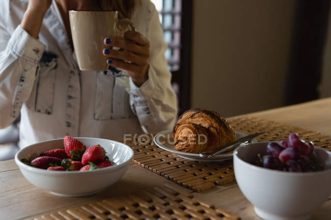 Sección media de la mujer tomando café en la cocina en casa - foto de stock