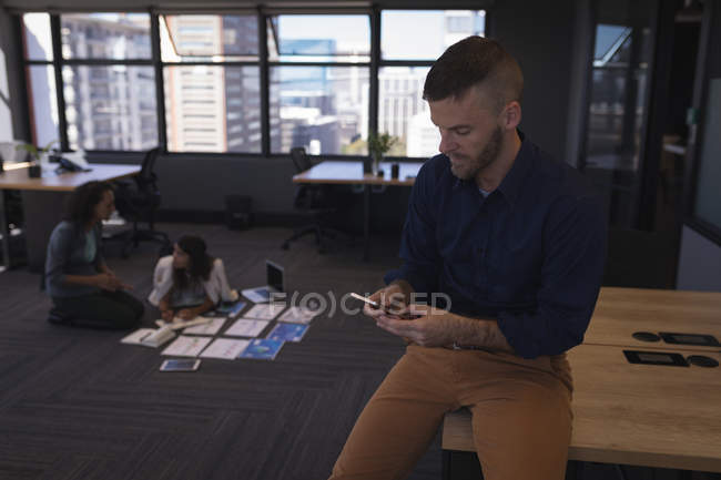 Empresário usando telefone enquanto outros discutem sobre documentos no escritório — Fotografia de Stock