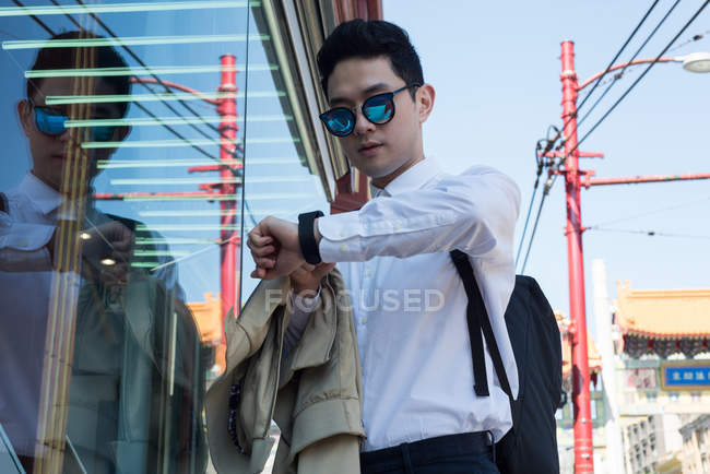 Молодой человек проверяет время во время прогулки по городской улице — стоковое фото