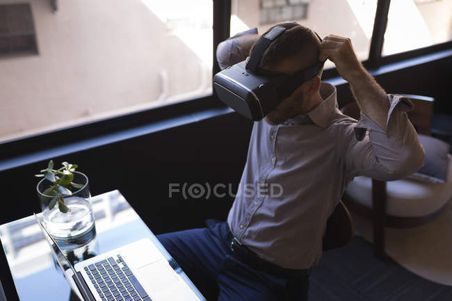 Businessman using virtual reality headset while working on laptop at office — Stock Photo